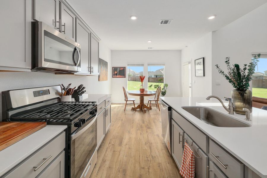 Modern kitchen featuring light gray cabinetry with brushed nickel hardware, stainless steel appliances, and light wood-finish flooring Modern kitchen featuring light gray cabinetry with brushed nickel hardware, stainless steel appliances, and light wood-finish flooring