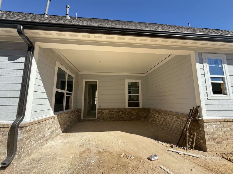 Entrance to property with brick siding, a patio area, and a shingled roof