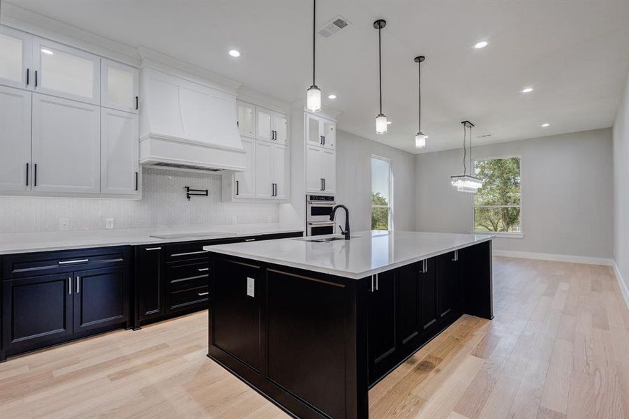 Open-concept kitchen featuring an expansive central island with a sink, white countertops, two-tone cabinetry, wood-finish flooring, and recessed lighting