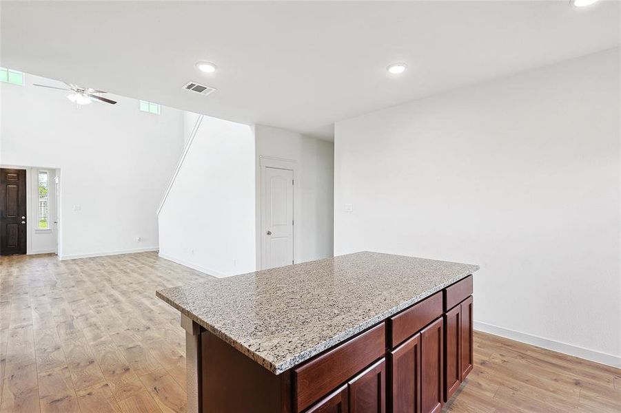 Kitchen featuring light hardwood / wood-style floors, a kitchen island, ceiling fan, and light stone counters