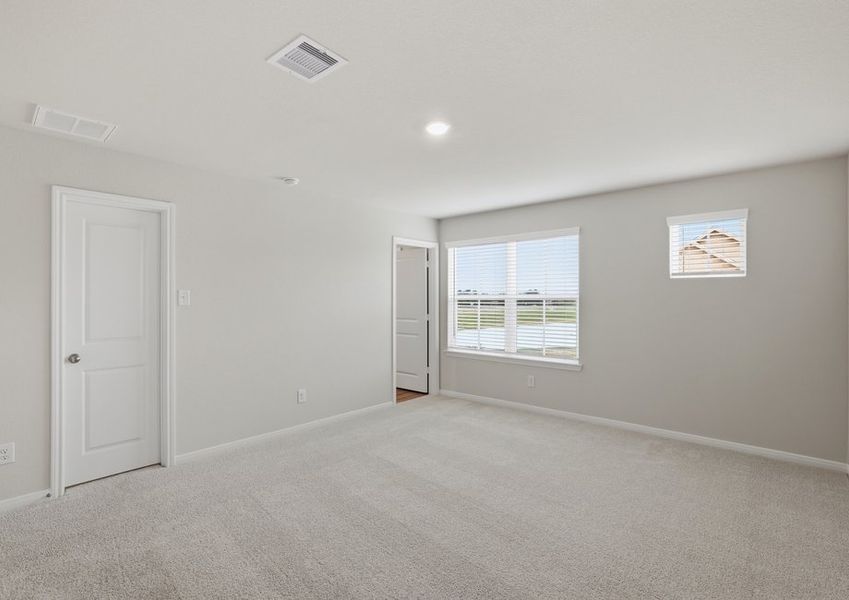 Spacious carpeted primary bedroom featuring a window with natural light and a door to the ensuite bath.