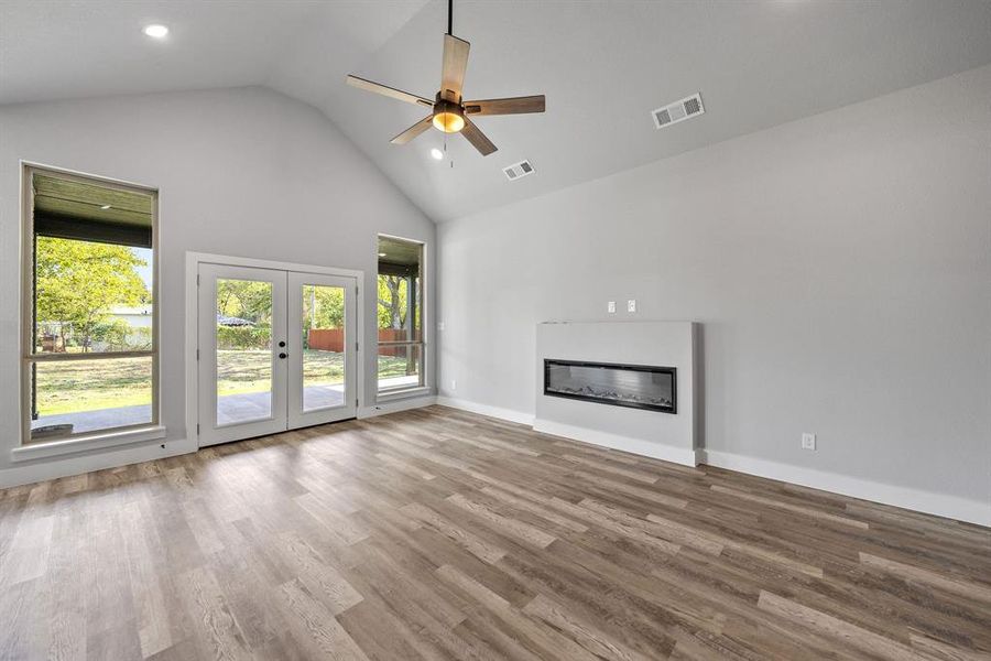 Unfurnished living room with a glass covered fireplace, high vaulted ceiling, light wood finished floors, french doors, and a ceiling fan