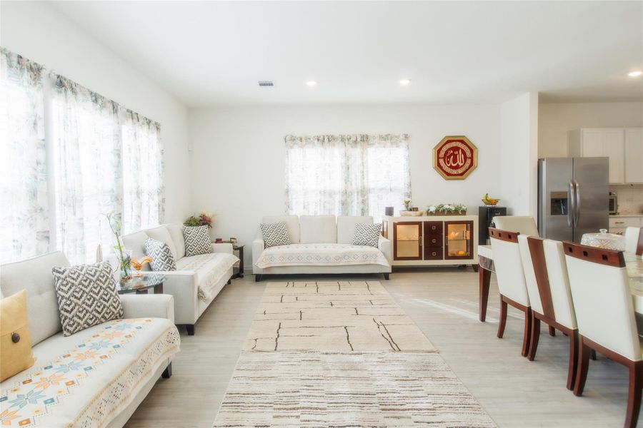 Bright and airy living room featuring large windows, wood-style floors, and recessed lighting, perfect for both relaxing and hosting guests.