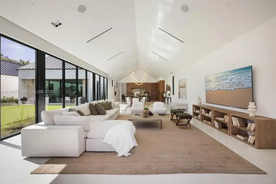 Vaulted ceilings featuring recessed linear lighting, floor-to-ceiling glass wall, built-in wooden media console, and integrated ceiling speakers
