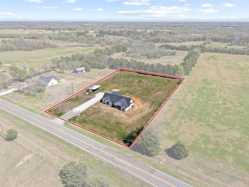 Aerial view of the property featuring a single-story home with a dark roof, a gravel driveway, and a covered carport