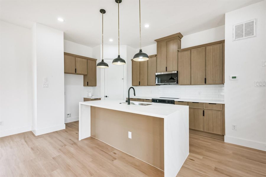 The kitchen features an island with a waterfall countertop, modern finishes, and soft wood cabinets.