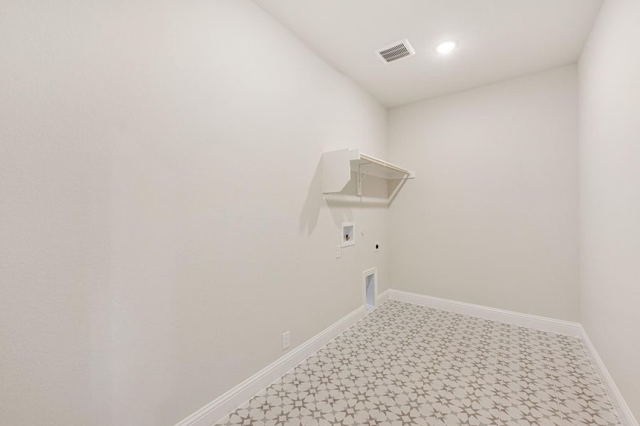 Empty laundry room with patterned tile floor, wall-mounted shelf, and washer and dryer hookups Empty laundry room with patterned tile floor, wall-mounted shelf, and washer and dryer hookups