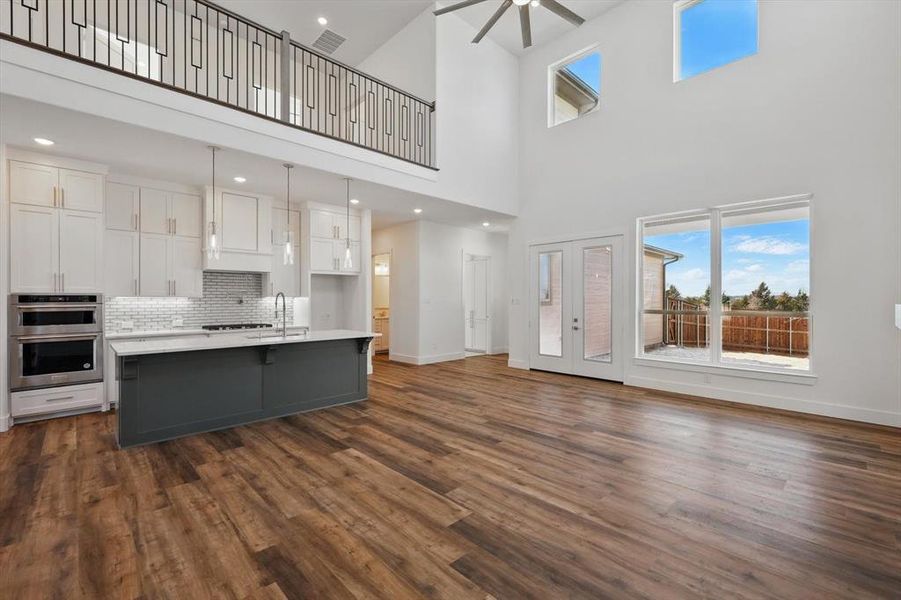 Kitchen with light countertops, stainless steel double oven, a center island with sink, and white cabinets