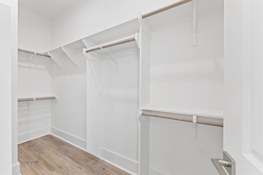 This photo showcases a spacious walk-in closet with wooden flooring and multiple hanging rods, providing ample storage space. The white walls enhance the brightness and openness of the area.