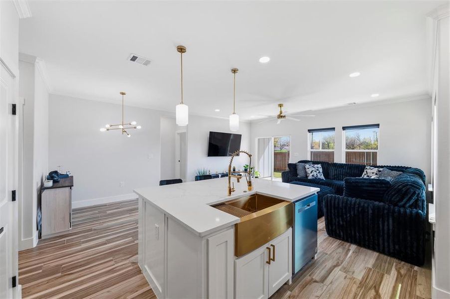 Kitchen with open floor plan, white cabinets, a kitchen island with sink, crown molding, and light wood-style flooring