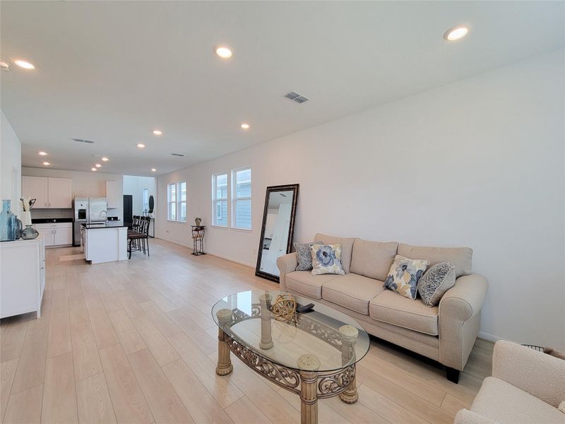 Spacious, open-concept living area with light wood flooring and a modern kitchen. There's ample natural light from large windows.