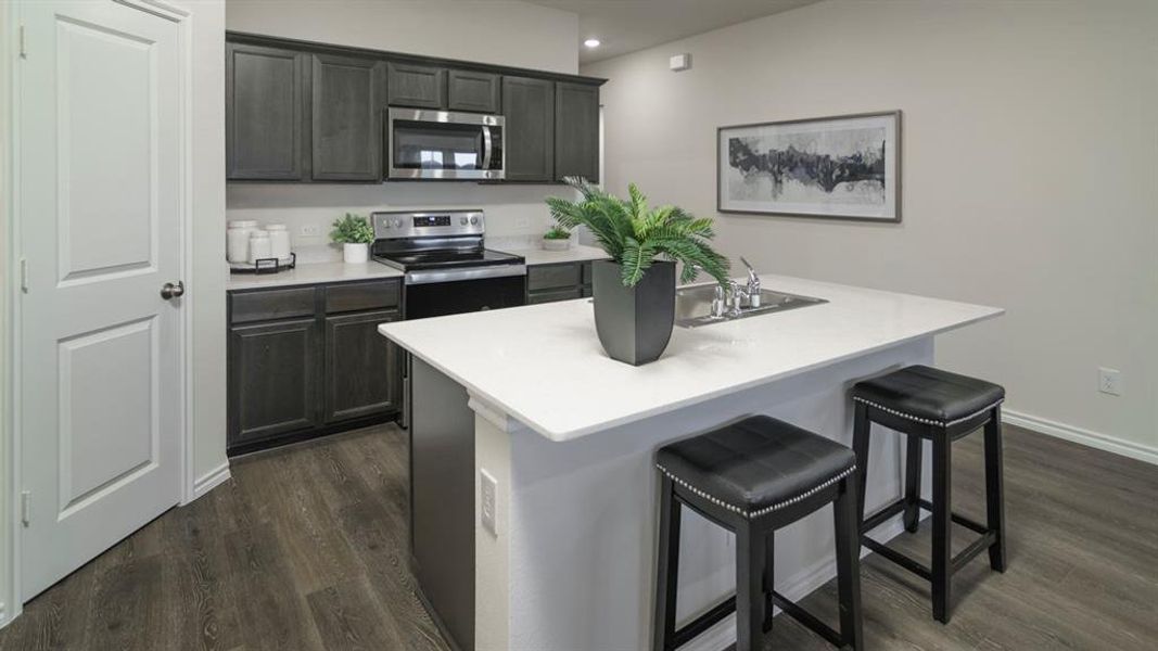 Kitchen featuring dark wood cabinetry, stainless steel appliances, a white solid surface island with an integrated sink, and wood-finish flooring Kitchen featuring dark wood cabinetry, stainless steel appliances, a white solid surface island with an integrated sink, and wood-finish flooring