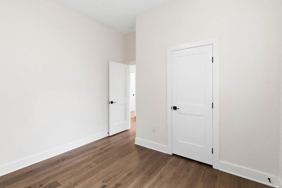 Bedroom 2 - Well-lit room featuring rich hardwood flooring and modern interior doors with black hardware. Bedroom 2 - Well-lit room featuring rich hardwood flooring and modern interior doors with black hardware.