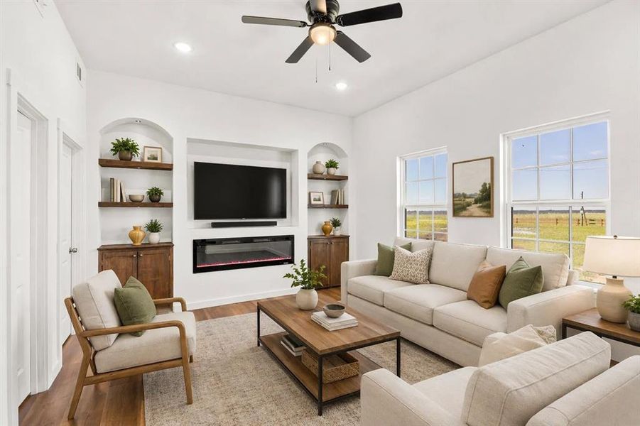 Vaulted ceiling living area featuring an integrated media center with an electric fireplace, two arched built-in shelving units, wood-finish flooring, and multiple large windows