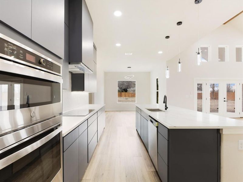 Dual tone kitchen featuring stainless steel appliances, modern cabinets, pendant lighting, two tone cabinets, and light wood-type flooring