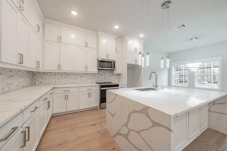 Kitchen with light stone countertops, hanging light fixtures, appliances with stainless steel finishes, a kitchen island with sink, and recessed lighting