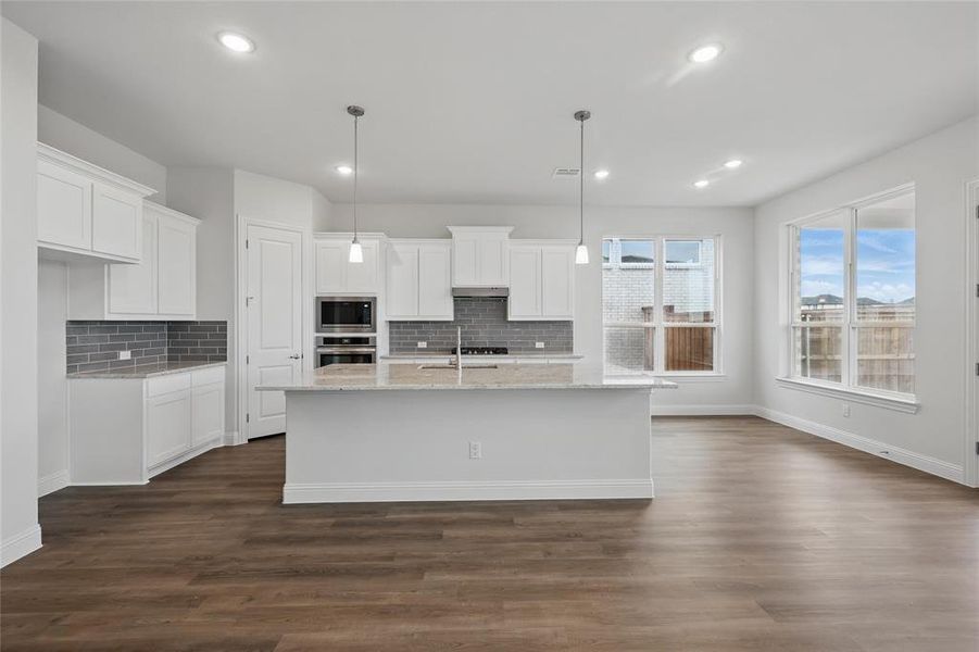Kitchen with white cabinetry, dark wood-style flooring, stainless steel appliances, a sink, and a kitchen island with sink