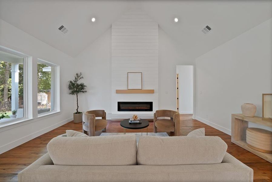 Living area featuring a fireplace, high vaulted ceiling, wood finished floors, and recessed lighting Living area featuring a fireplace, high vaulted ceiling, wood finished floors, and recessed lighting