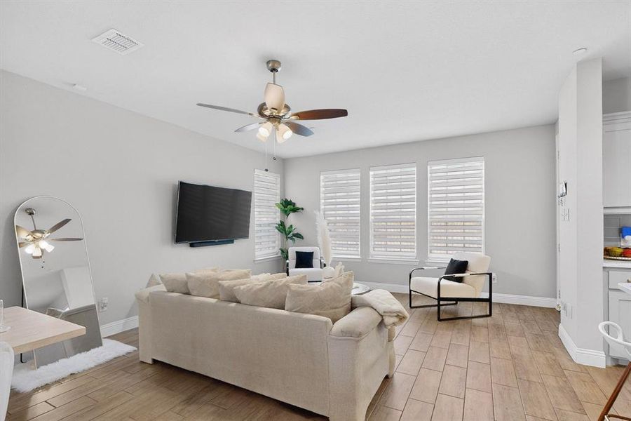 Living room featuring light-toned walls, a ceiling fan, and three windows with blinds