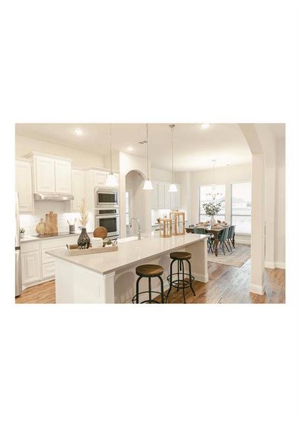 Kitchen featuring a large island, stainless steel appliances, a kitchen breakfast bar, white cabinets, and decorative light fixtures