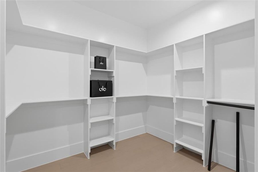 Walk-in closet featuring white built-in shelving, multiple storage compartments, a corner configuration, and a hanging rod