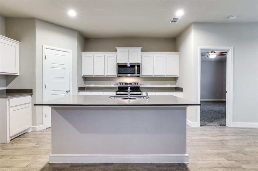 Kitchen with stainless steel appliances, white cabinetry, light wood finished floors, a center island with sink, and recessed lighting Kitchen with stainless steel appliances, white cabinetry, light wood finished floors, a center island with sink, and recessed lighting