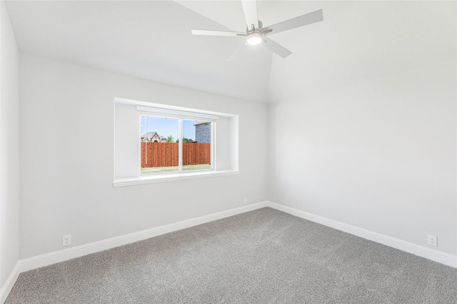 Empty bedroom with vaulted ceiling, ceiling fan, carpet flooring, and single window overlooking backyard fence