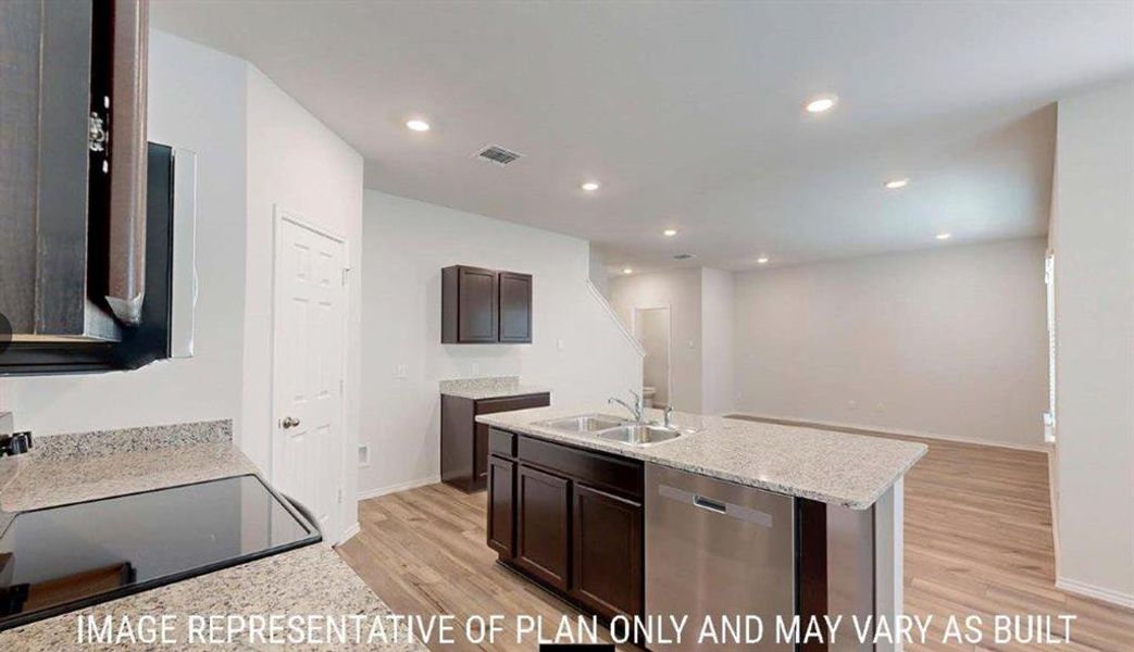 Contemporary kitchen featuring wood-finish flooring, recessed lighting, an island with a double basin sink, stainless steel dishwasher, and light-colored countertops Contemporary kitchen featuring wood-finish flooring, recessed lighting, an island with a double basin sink, stainless steel dishwasher, and light-colored countertops