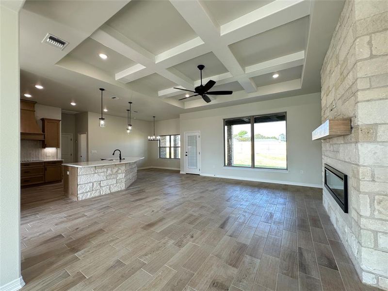 Unfurnished living room featuring wood finish floors, a fireplace, coffered ceiling, a ceiling fan, and beamed ceiling