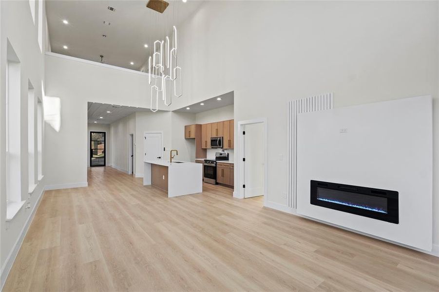 Unfurnished living room with a glass covered fireplace, a sink, light wood-style flooring, and a high ceiling