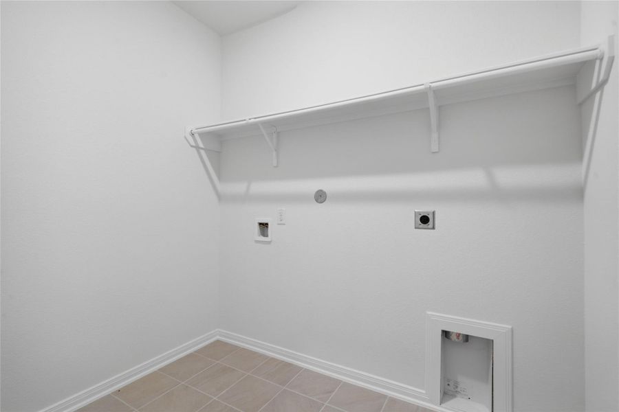 The conveniently located laundry room offers a practical workspace with shelf, tile flooring, and plenty of room for your appliances.