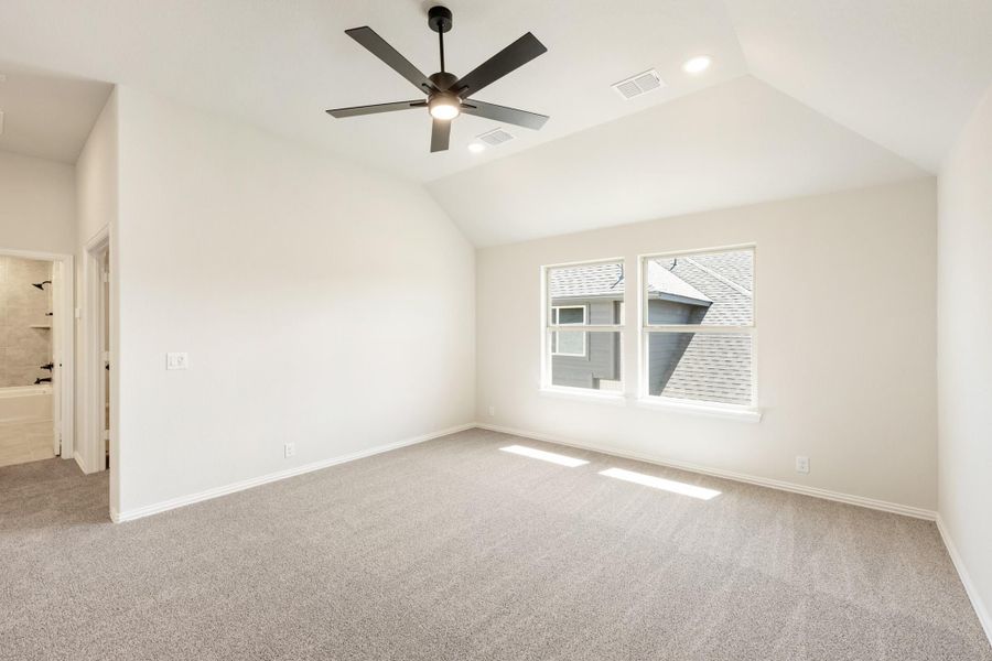 Empty bedroom with vaulted ceiling, ceiling fan, carpet flooring, and ensuite bathroom doorway
