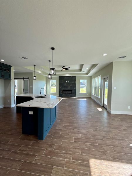 This spacious open-concept living area features a modern kitchen with a large island, stylish pendant lighting, and wood-look tile flooring. A cozy fireplace sits between large windows offering plenty of natural light, creating an inviting atmosphere. This spacious open-concept living area features a modern kitchen with a large island, stylish pendant lighting, and wood-look tile flooring. A cozy fireplace sits between large windows offering plenty of natural light, creating an inviting atmosphere.