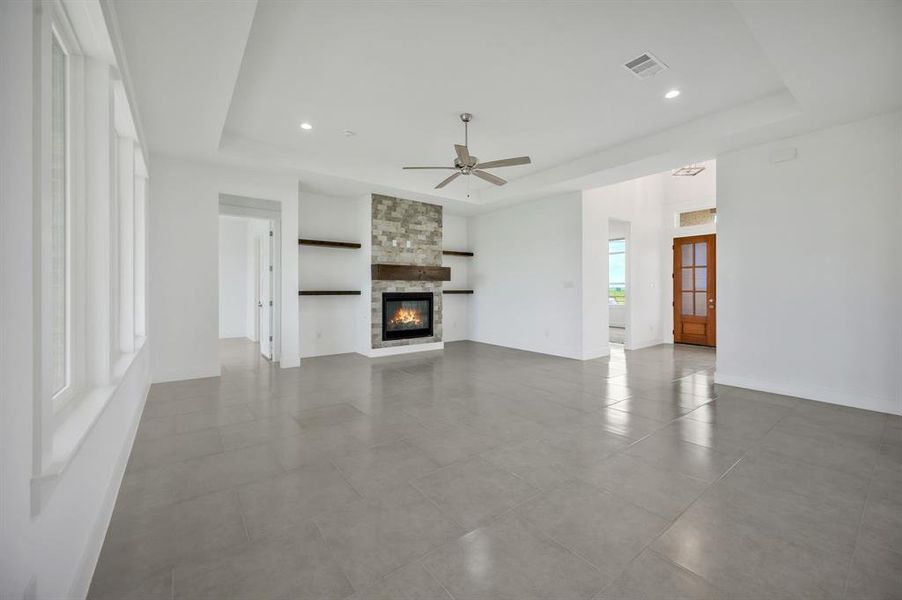 Unfurnished living room featuring ceiling fan, a fireplace, a tray ceiling, and visible vents Unfurnished living room featuring ceiling fan, a fireplace, a tray ceiling, and visible vents