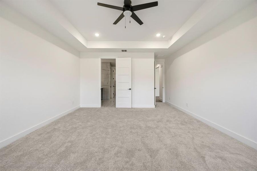 Spacious interior room featuring light gray carpeting, crisp white walls, and a recessed tray ceiling Spacious interior room featuring light gray carpeting, crisp white walls, and a recessed tray ceiling
