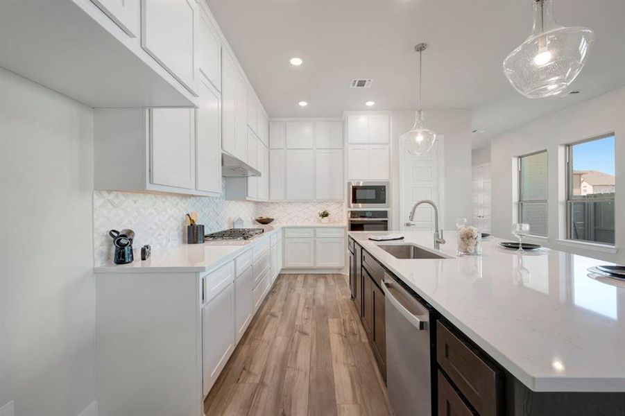 Two tone kitchen with two tone cabinetry, light wood finished floors, stainless steel appliances, light stone countertops, and tasteful backsplash