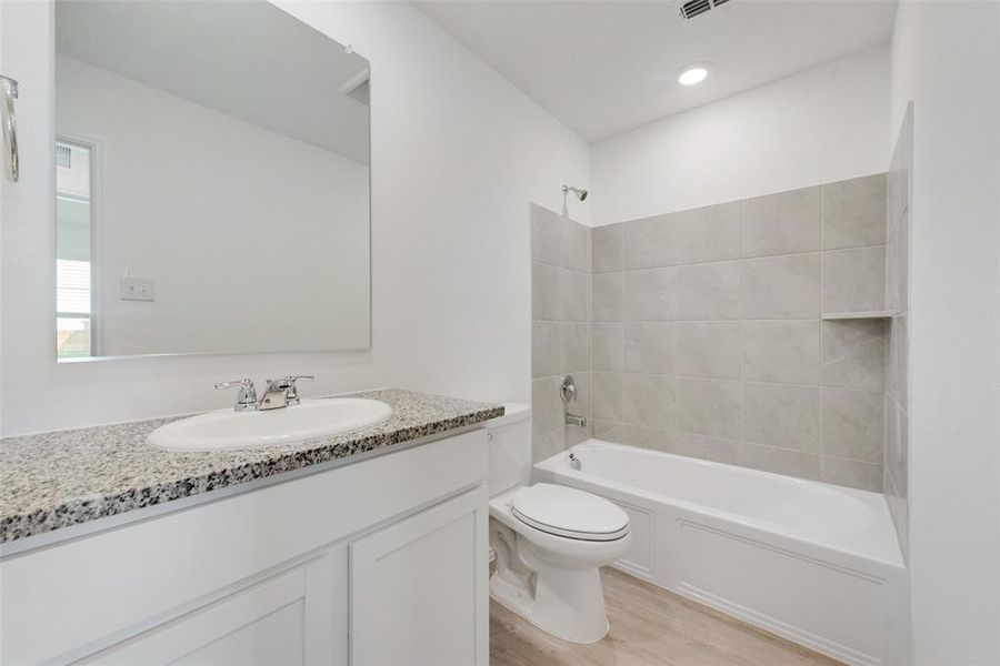 Full bathroom with vanity, tiled shower / bath combo, toilet, and hardwood / wood-style flooring