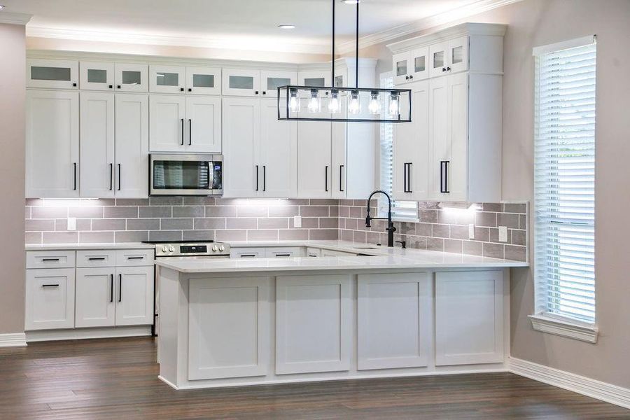 Kitchen with healthy amount of natural light, decorative backsplash, stainless steel microwave, glass insert cabinets, and ornamental molding Kitchen with healthy amount of natural light, decorative backsplash, stainless steel microwave, glass insert cabinets, and ornamental molding
