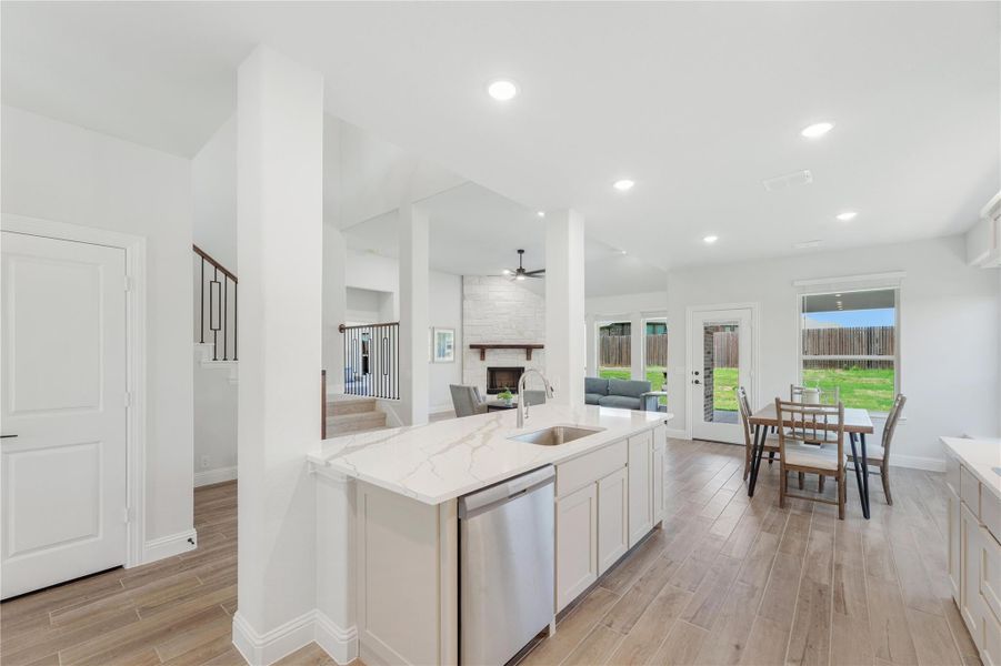 Kitchen island with quartz countertop and sink open to dining area and living room with fireplace and wood-look floors Kitchen island with quartz countertop and sink open to dining area and living room with fireplace and wood-look floors