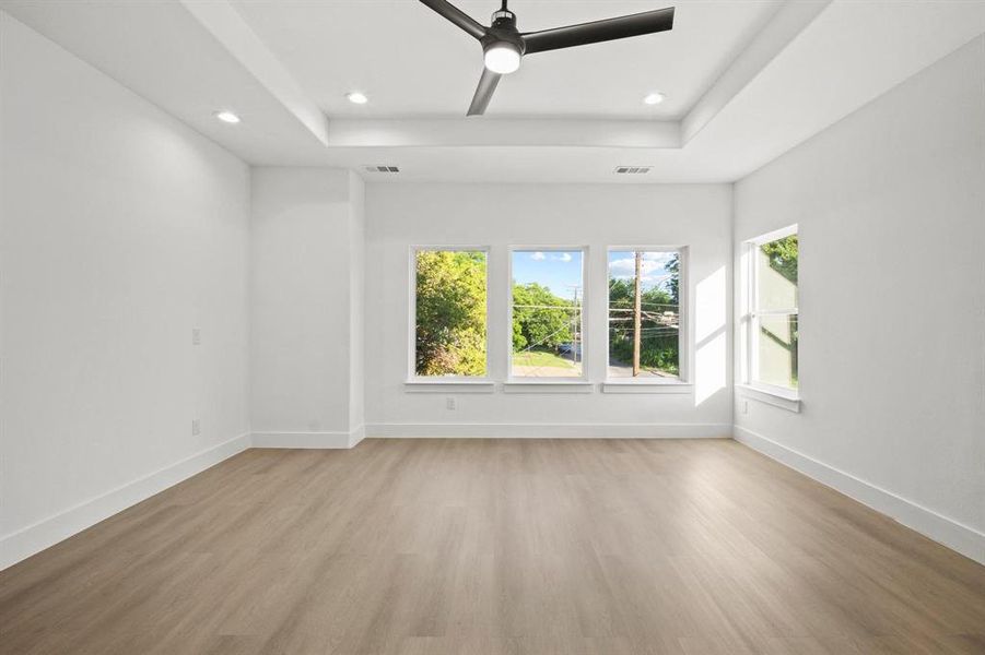 Empty room featuring a tray ceiling, light wood-style floors, healthy amount of natural light, ceiling fan, and recessed lighting