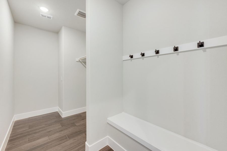 Mudroom with built-in bench, coat hooks, and wood-look flooring leading to a walk-in closet Mudroom with built-in bench, coat hooks, and wood-look flooring leading to a walk-in closet