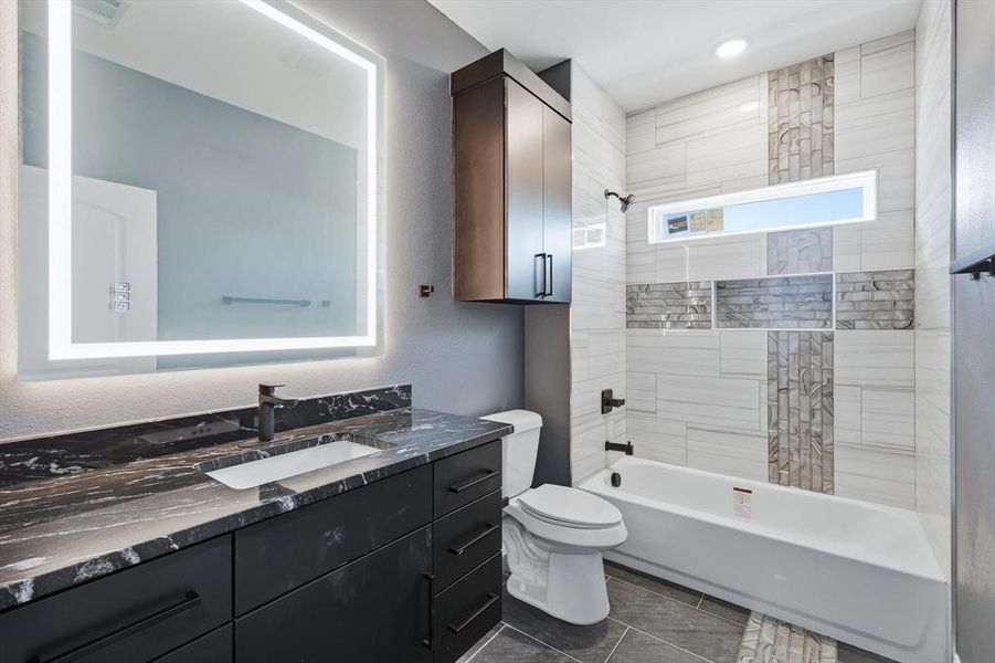 Bathroom with a textured wall, vanity, shower / bath combination, and dark tile patterned floors