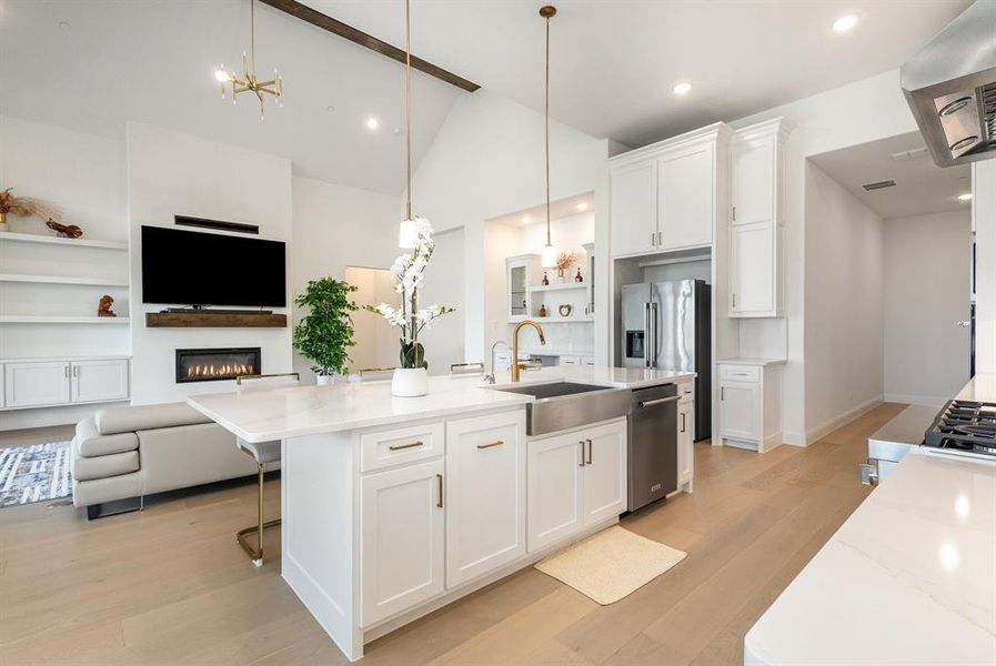 Kitchen with open floor plan, white cabinets, light stone counters, range hood, and high vaulted ceiling