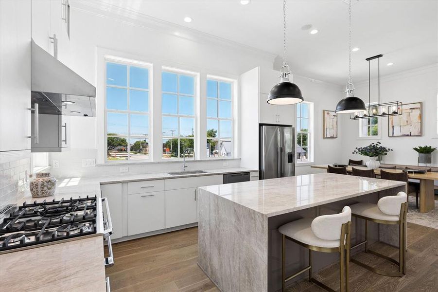 Gourmet kitchen featuring a waterfall island with stone countertop, stainless steel appliances, white cabinetry, and wood-finish flooring