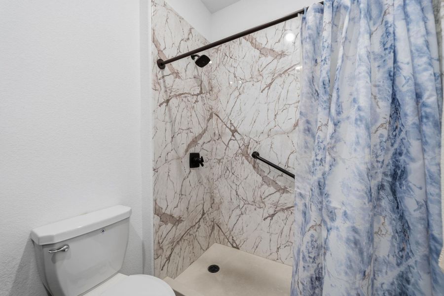 Walk-in shower with full-height marble-patterned wall panels, black shower fixtures, and a grab bar