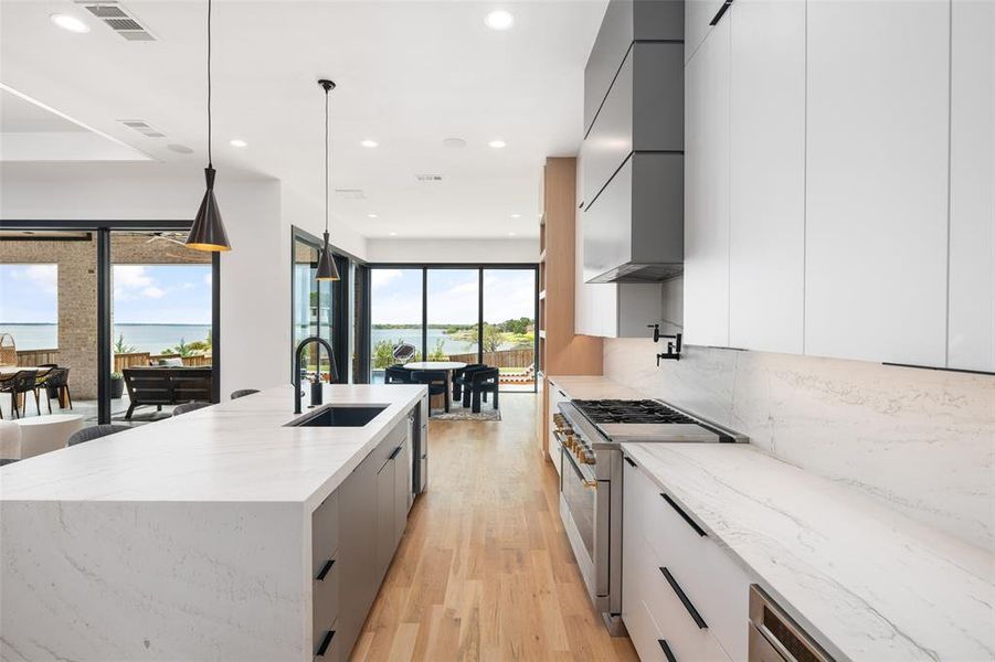 Gourmet kitchen featuring premium Monogram appliances, sleek custom cabinetry, and elegant Taj Mahal quartzite countertops. Real hardwood floors flow throughout the space, while expansive glass doors frame breathtaking lake views, bringing natural light and the beauty of the outdoors into the heart of the home.