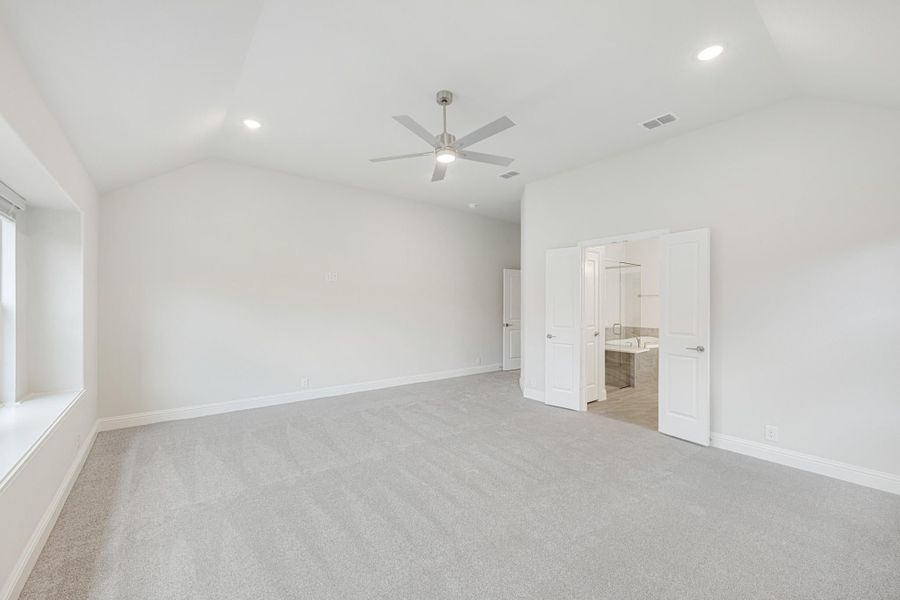 Empty bedroom with vaulted ceiling, ceiling fan, gray carpet, and open ensuite bathroom doorway Empty bedroom with vaulted ceiling, ceiling fan, gray carpet, and open ensuite bathroom doorway