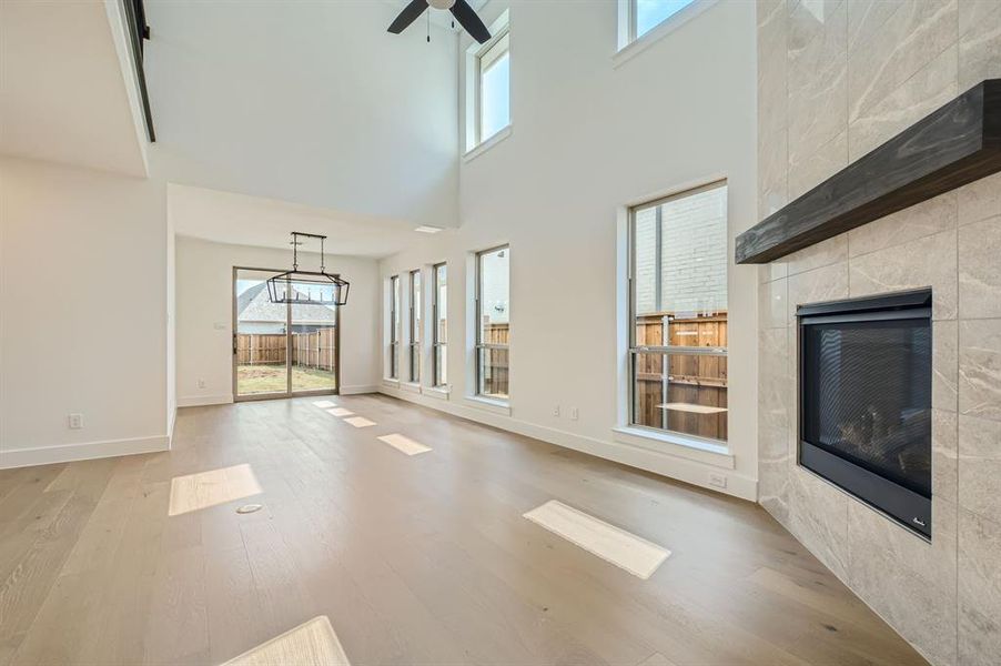 Unfurnished living room featuring a tile fireplace, a high ceiling, ceiling fan with notable chandelier, and light hardwood / wood-style flooring