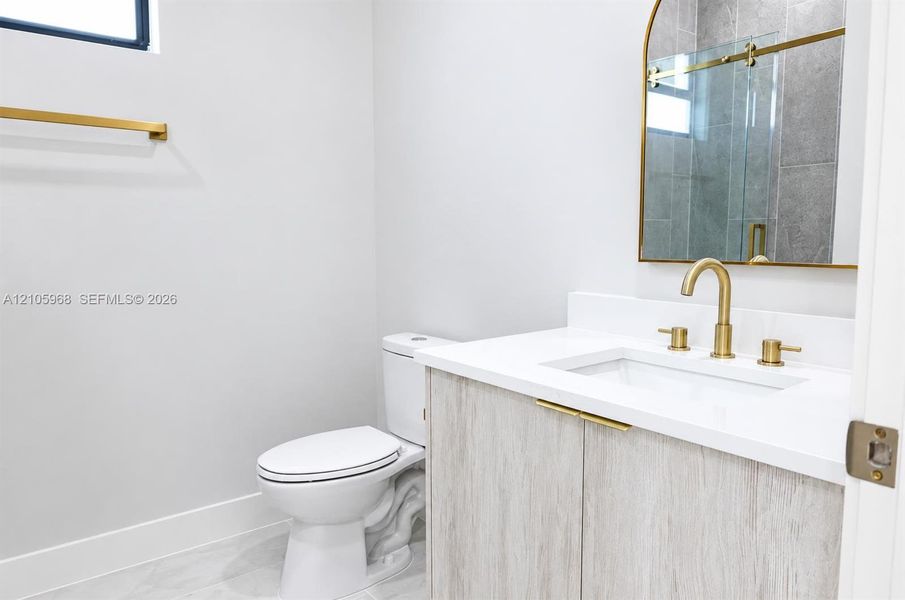 Vanity featuring light wood-finish cabinetry, a white countertop with an integrated rectangular sink, brass hardware, an arched mirror, and a wall-mounted faucet
