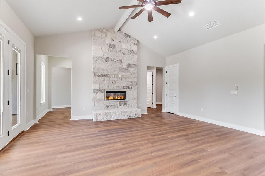 Unfurnished living room featuring a ceiling fan, light wood-style floors, and a stone fireplace